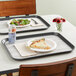 A Dinex woodgrain tray with a pizza and salad on it on a table.