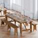 A Lancaster Table & Seating Vineyard Series long wooden table with two wooden benches set up outside with plates and glasses.