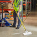 A man wearing a safety vest and using a Midwest Rake stainless steel scraper on a floor.