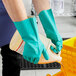 A person in green Midwest Rake Solvent-Resistant Nitrile gloves holding a jug of cleaning liquid.