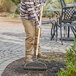 A person using a Seymour steel bow rake with a wooden handle to clean the ground.