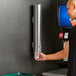 A man using a ServSense stainless steel cup dispenser on a white wall.