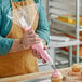 A person using a Choice clear disposable pastry bag to pipe pink icing onto a cupcake.