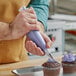 A person using a Choice clear disposable pastry bag to pipe purple frosting onto a cupcake.