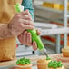A hand using a green Choice pastry bag to frost a cupcake.