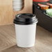 A white Choice double wall paper hot cup with a black lid on a counter.