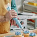 A man using a Choice clear disposable pastry bag to pipe blue frosting onto a cupcake.