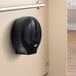 A black Lavex single roll toilet paper dispenser with a round hole on a wall.