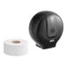A black Lavex jumbo single roll toilet paper dispenser on a counter with a roll of toilet paper next to it.
