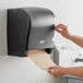 A person using a Lavex black lever-activated paper towel dispenser.