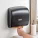 A hand using a Lavex translucent black mini multifold paper towel dispenser.