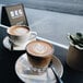 Two cups of BKG Heritage whole bean coffee on a table with a leaf design in the foam.