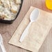 A white Berk heavy weight plastic teaspoon next to a bowl of potato salad.