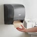 A hand reaching out to a black Lavex automatic paper towel dispenser.