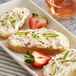 A plate with bread and strawberries next to a container of Don's Salads Horseradish and Chives Cheddar Cheese Spread.