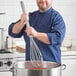 A man in a chef's uniform using a Fourté stainless steel French whisk in a pot.