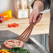 A hand holding a brown Mercer Culinary Hell's Tools spatula over a pan of food.