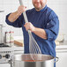 A man in a chef's uniform using a Fourt&#233; stainless steel whisk in a pot.