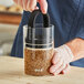 A person using a Prepara Evak Classic glass food storage container to pour seeds into it.
