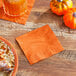 A plate of pie and a glass of orange juice on a table with an orange beverage napkin.