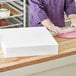 A person wearing a purple shirt and gloves cuts a rectangular foam cake dummy.