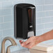 A person using a Lavex black manual liquid soap dispenser.