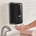 A person using a black Lavex automatic foaming soap dispenser.