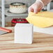 A close-up of a person's hand cutting a white foam cube.