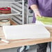 A person using a sponge to put on a rectangular foam cake dummy.