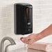 A person using a black Lavex automatic foaming soap dispenser.