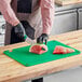 A person cutting a watermelon on a green Choice cutting board.