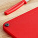 A red Choice cutting board with black grips and rulers on a wood surface.