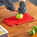 A person in black gloves cutting a lime on a red Choice cutting board.