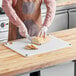 A person using a Choice white cutting board with rulers to cut bread on a counter.