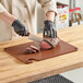 A person cutting meat on a Choice brown cutting board.