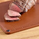 A piece of meat on a Choice brown cutting board with rulers and grips.