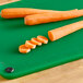 A green Choice cutting board with sliced carrots on it.