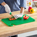 A person in gloves cutting red and yellow bell peppers on a Choice green cutting board.