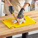 A person in gloves using a knife to cut a chicken on a yellow Choice cutting board.