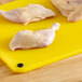 A yellow Choice cutting board with raw chicken on it.