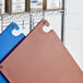 A brown Choice cutting board with grips, hooks, and rulers on a shelf with spices.