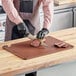 A person in black gloves cutting meat on a Choice brown cutting board.