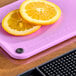 A purple Choice cutting board with slices of oranges on it.