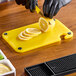 A person slicing a lemon on a Choice yellow cutting board.