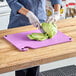 A woman cutting lettuce on a purple Choice cutting board.
