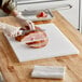 A person cutting meat on a white Choice cutting board.