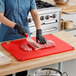 A woman cutting meat on a Choice red cutting board on a counter.
