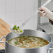 A person using a Choice stainless steel skimmer to stir a pot of soup.