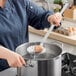 A person using the Choice stainless steel skimmer to cook in a pot.