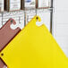 A yellow rectangular Choice cutting board with grips and rulers on a brown surface with a hook.